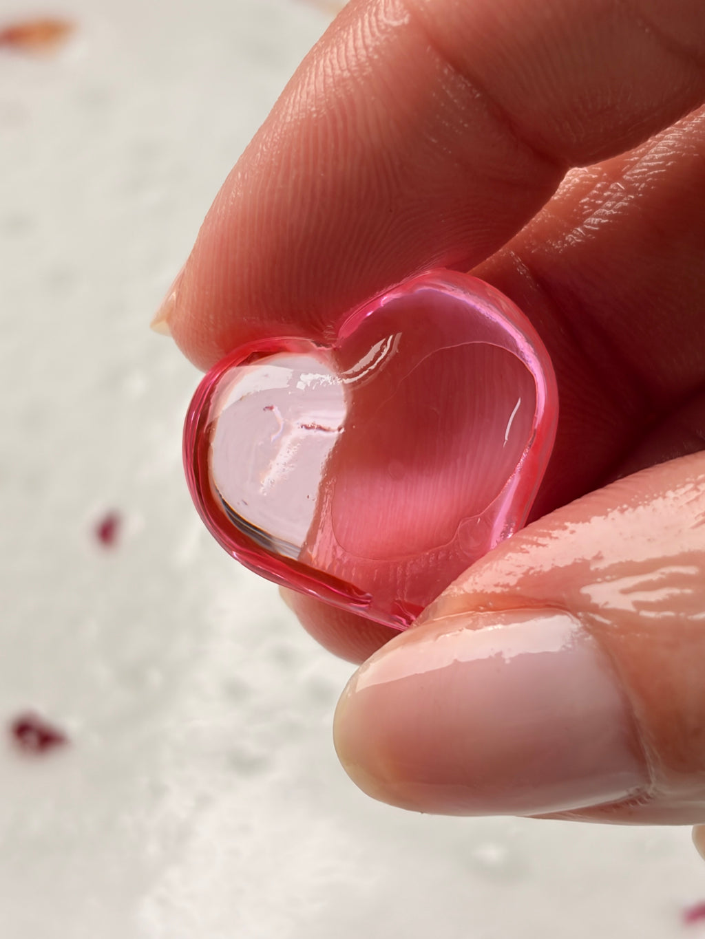 Hand holding a small pink heart-shaped object against a light background