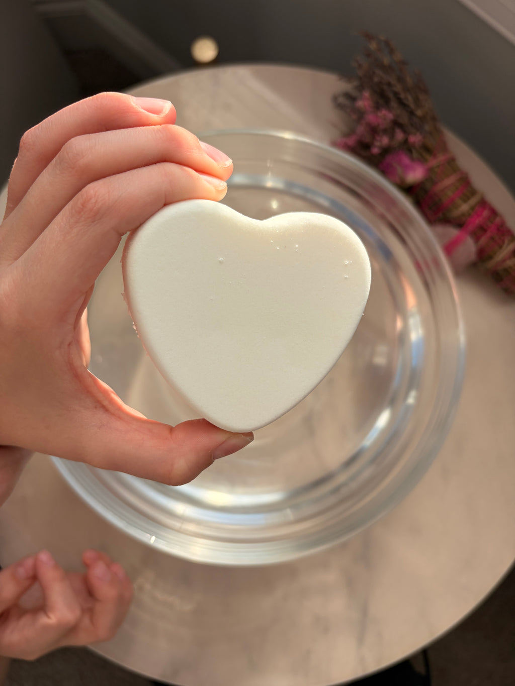 sensitive skin-friendly heart-shaped white bath bomb held by a hand with a blurred background